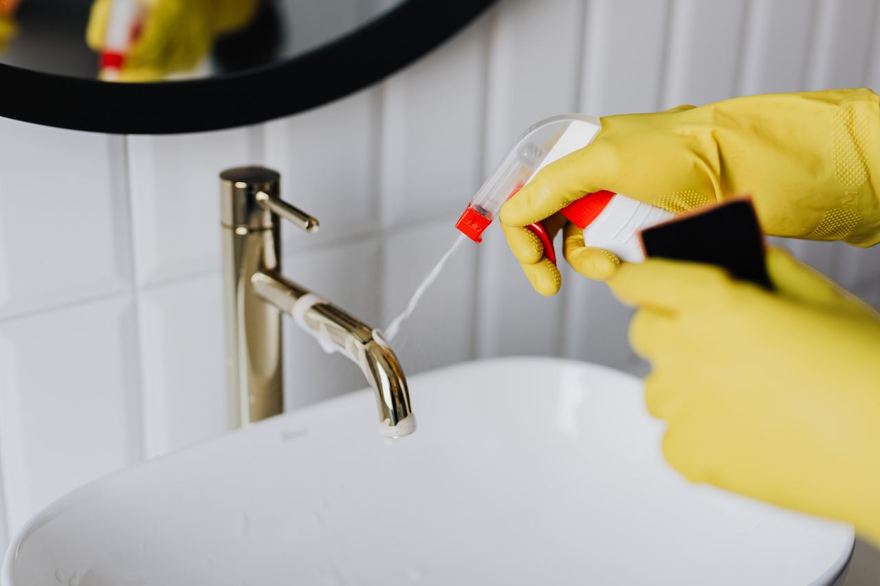 project-01-d From above anonymous housekeeper in yellow rubber gloves spraying cleaner to chrome water faucet in bathroom